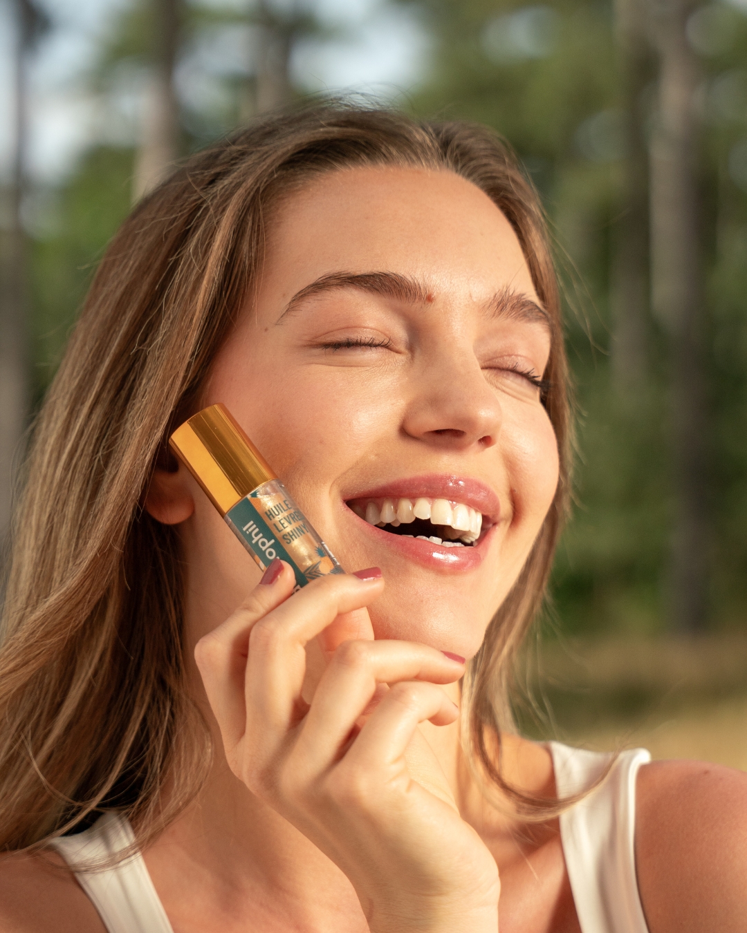 jeune femme souriante qui tient dans sa main l'huile à lèvres dermophil shiny